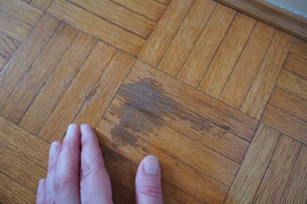 A close-up of a dark water stain and stripped protective finish on a natural oak